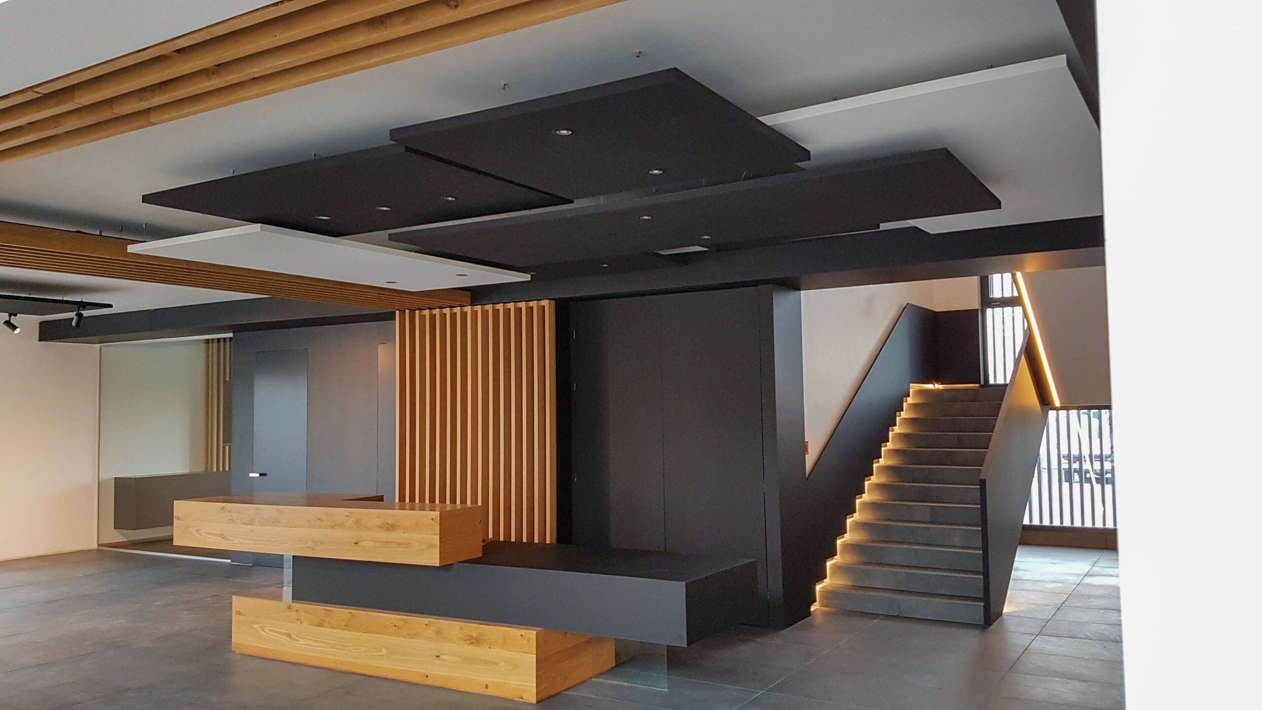 Empfangsbereich Bürogebäude, Theke, Schwarz, Holztöne, Decken und Wandelemente, Stiegenaufgang